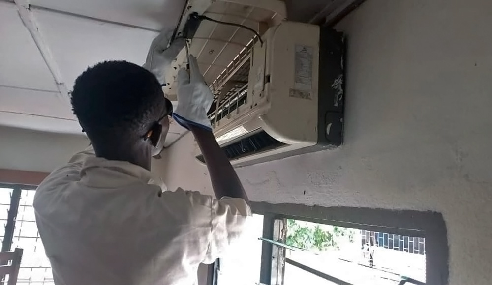 Mamadou répare une climatisation dans les locaux d'une entreprise.